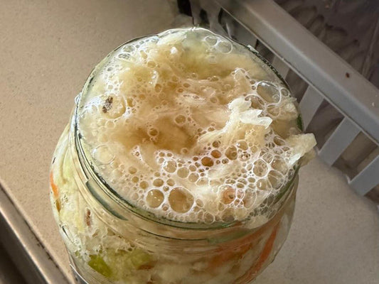 Fresh sauerkraut actively fermenting in a glass jar, bubbles rising through the brine - a sign it's alive and keeps best in the fridge.